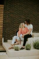 Smiling young couple in love sitting in front of house brick wall photo