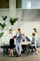 Two young business women looking at financial results on digital tablet in front of their team at the office photo