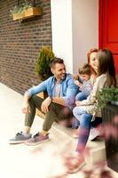 Family with a mother, father, son and daughter sitting outside on the steps of a front porch of a brick house photo