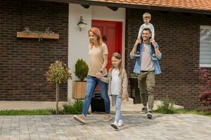 Family with a mother, father, son and daughter walking with baggage outside on the front porch of a brick house photo