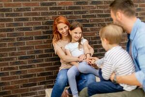 Family with a mother, father, son and daughter sitting outside on the steps of a front porch of a brick house photo