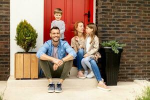 Family with a mother, father, son and daughter sitting outside on the steps of a front porch of a brick house photo