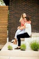 Smiling young couple in love sitting in front of house brick wall photo