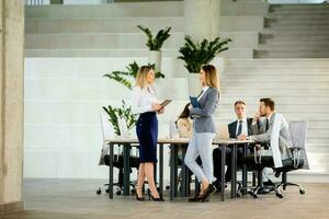 Two young business women looking at financial results on digital tablet in front of their team at the office photo