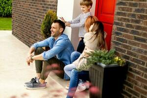 Family with a mother, father, son and daughter sitting outside on the steps of a front porch of a brick house photo