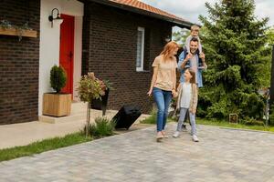 Family with a mother, father, son and daughter walking with baggage outside on the front porch of a brick house photo