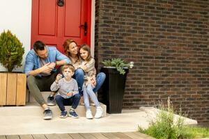 Family with a mother, father, son and daughter sitting outside on the steps of a front porch of a brick house photo