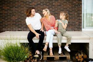 Family with a mother, father and daughter sitting outside on the steps of a front porch of a brick house photo