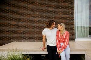 Smiling young couple in love sitting in front of house brick wall photo