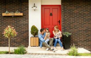 Family with a mother, father, son and daughter sitting outside on the steps of a front porch of a brick house photo