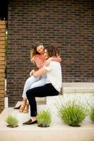 Smiling young couple in love sitting in front of house brick wall photo