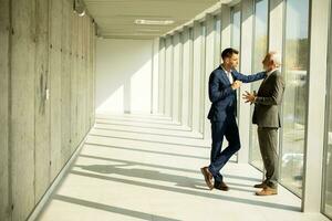 Mature businessman and his young colleague discussing in the office corridor photo