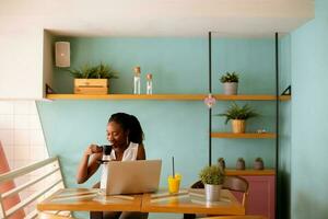 Young black woman drinking coffee  while working on laptop in the cafe photo