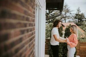 Smiling young couple in love dancing in front of house brick wall photo