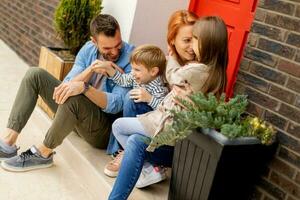 Family with a mother, father, son and daughter sitting outside on the steps of a front porch of a brick house photo