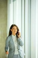 joven mujer utilizando móvil teléfono por el oficina ventana foto