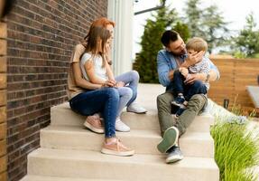 Family with a mother, father, son and daughter sitting outside on the steps of a front porch of a brick house photo