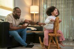 Happy African American man playing with his daughter in living room at home photo