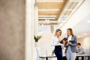 Two young business women looking at financial results on digital tablet in front of their team at the office photo