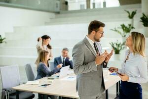 Young business couple looking at financial results on digital tablet in front of their team at the office photo