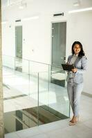 Young business woman using mobile phone in the office hallway photo