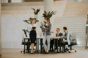 Two young business women looking at financial results on digital tablet in front of their team at the office photo