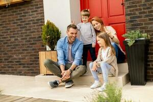 Family with a mother, father, son and daughter sitting outside on the steps of a front porch of a brick house photo