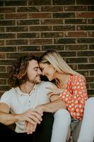 Smiling young couple in love sitting in front of house brick wall photo