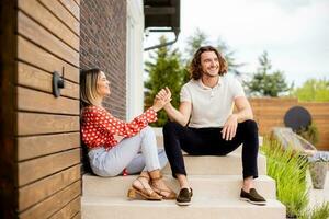 sonriente joven Pareja en amor sentado en frente de casa ladrillo pared foto