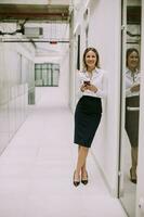 Young business woman using mobile phone in the office hallway photo