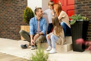 Family with a mother, father, son and daughter sitting outside on the steps of a front porch of a brick house photo