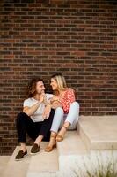 Smiling young couple in love sitting in front of house brick wall photo