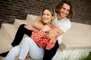 Smiling young couple in love sitting in front of house brick wall photo