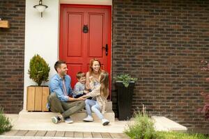 Family with a mother, father, son and daughter sitting outside on the steps of a front porch of a brick house photo