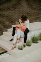 Smiling young couple in love sitting in front of house brick wall photo