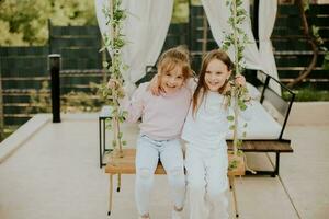 Cute little girls on the swing in the house backyard photo