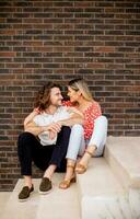 Smiling young couple in love sitting in front of house brick wall photo