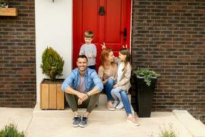 Family with a mother, father, son and daughter sitting outside on the steps of a front porch of a brick house photo