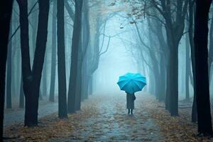 Woman under blue umbrella walks in the park on a foggy day. Generative AI photo