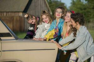 Young cheerful girls are pushing an old car. Women in the style of the 90s. photo