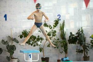 A child in a cap and swimming goggles jumps into the pool. Swimming section. photo