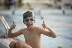 chico en un nadando gorra y nadando gafas de protección en el piscina. el niño es comprometido en el nadando sección. foto