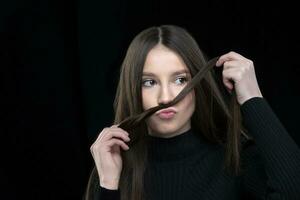 A beautiful girl with long hair fooling around in front of the camera. Makes a mustache out of hair. photo