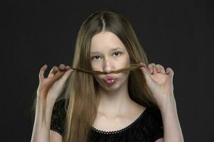 hermosa Adolescente niña engañando alrededor en frente de el cámara. ella hace un Bigote fuera de su cabello. foto