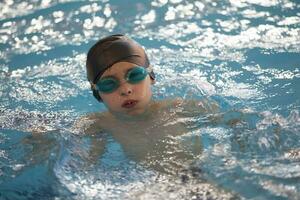 Boy in a swimming cap and swimming goggles in the pool. The child is engaged in the swimming section. photo