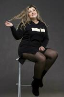 un hermosa grasa mujer con largo Rizado pelo se sienta en un silla. foto