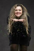 A beautiful fat woman with long curly hair and in a black dress blows sequins off her hands. photo