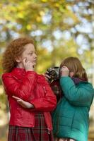 dos Pelirrojo muchachas novias fotografía cada otro en el otoño parque con un retro cámara. foto