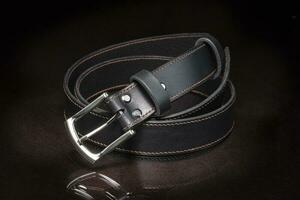 negro cuero cinturón con un metal hebilla en un oscuro antecedentes de cerca. foto