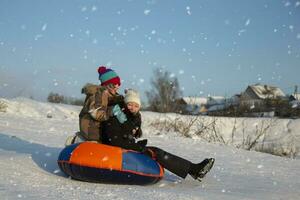 en un invierno día, niños Vamos trineo y risa alegremente. un chico y un niña Vamos abajo el montaña en un trineo. niños en el invierno en el pueblo en vacaciones. foto